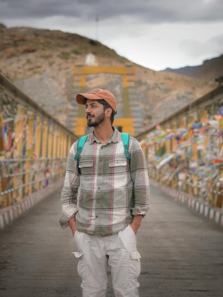 A man stands on a decorated bridge in a mountainous area, capturing a sense of adventure and travel.