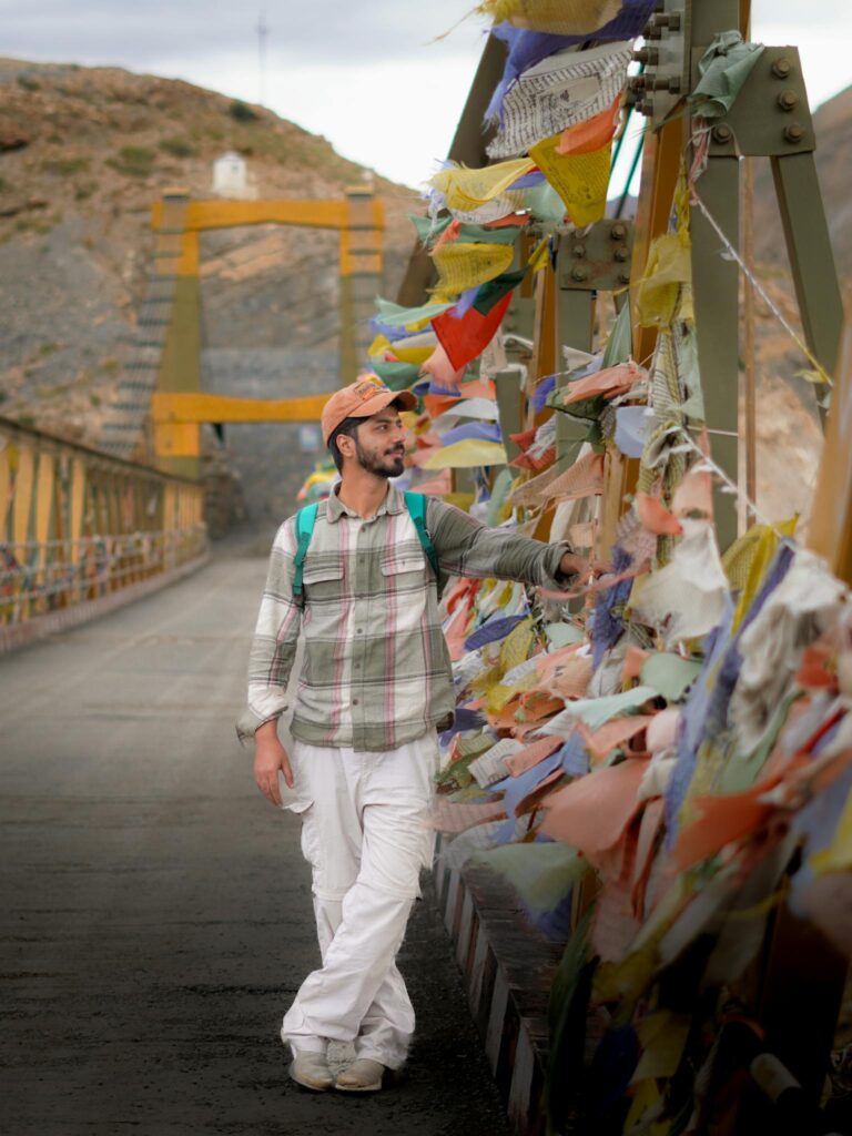 A man touches colorful prayer flags on a mountainous bridge, exuding a sense of adventure and serenity.