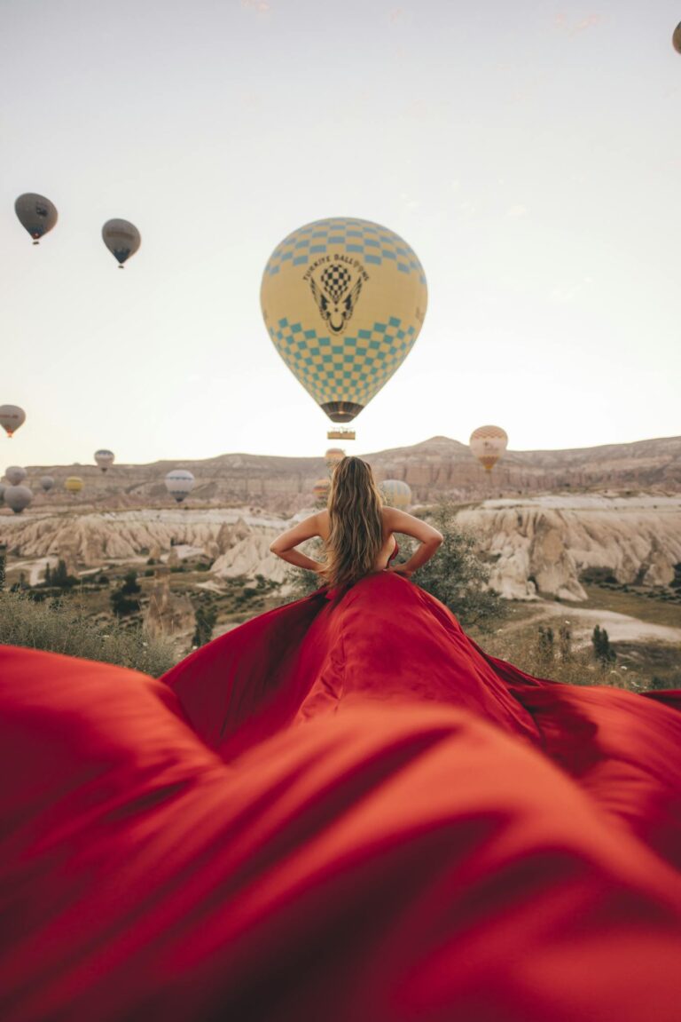 Back view of a woman in Cappadocia, Turkey, gazing at hot air balloons during sunrise.